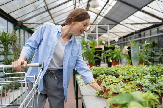Le concept du jardinage, de la plantation et du shopping. Une belle femme adulte choisit des plantes et des pots d'intérieur dans une serre ou un jardin. La dame achète des fleurs dans le magasin du centre commercial et choisit de grimper du lierre