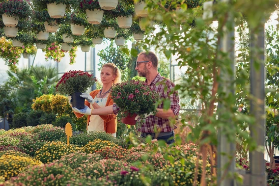 Une femme du jardin montre des fleurs aux clients souriants qui achètent des plantes